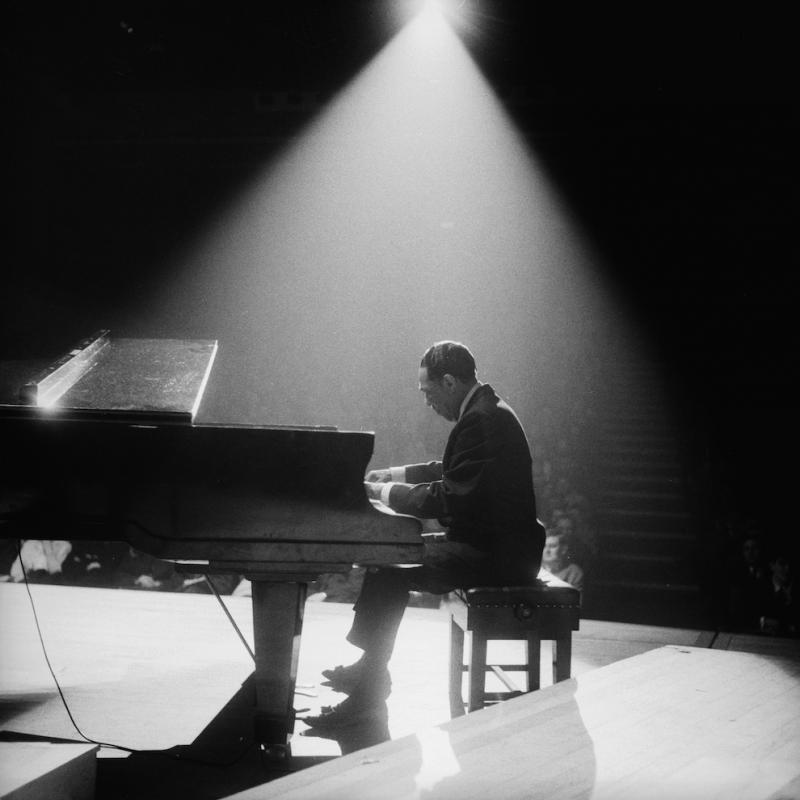 Jazz legend Duke Ellington playing the piano in a spotlight at a concert hall