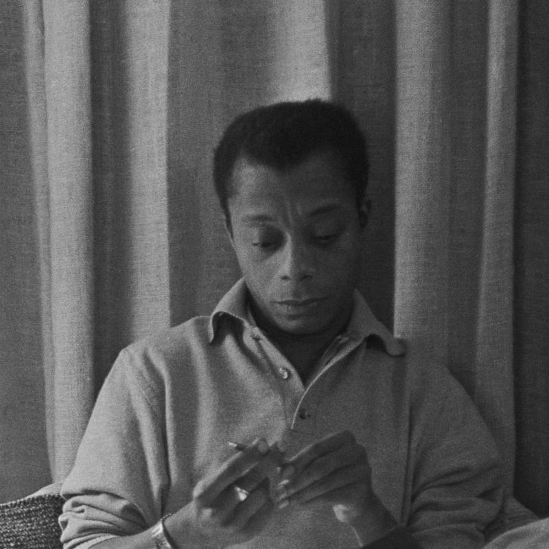 Writer and activist James Baldwin looks down at an object in his hands 
